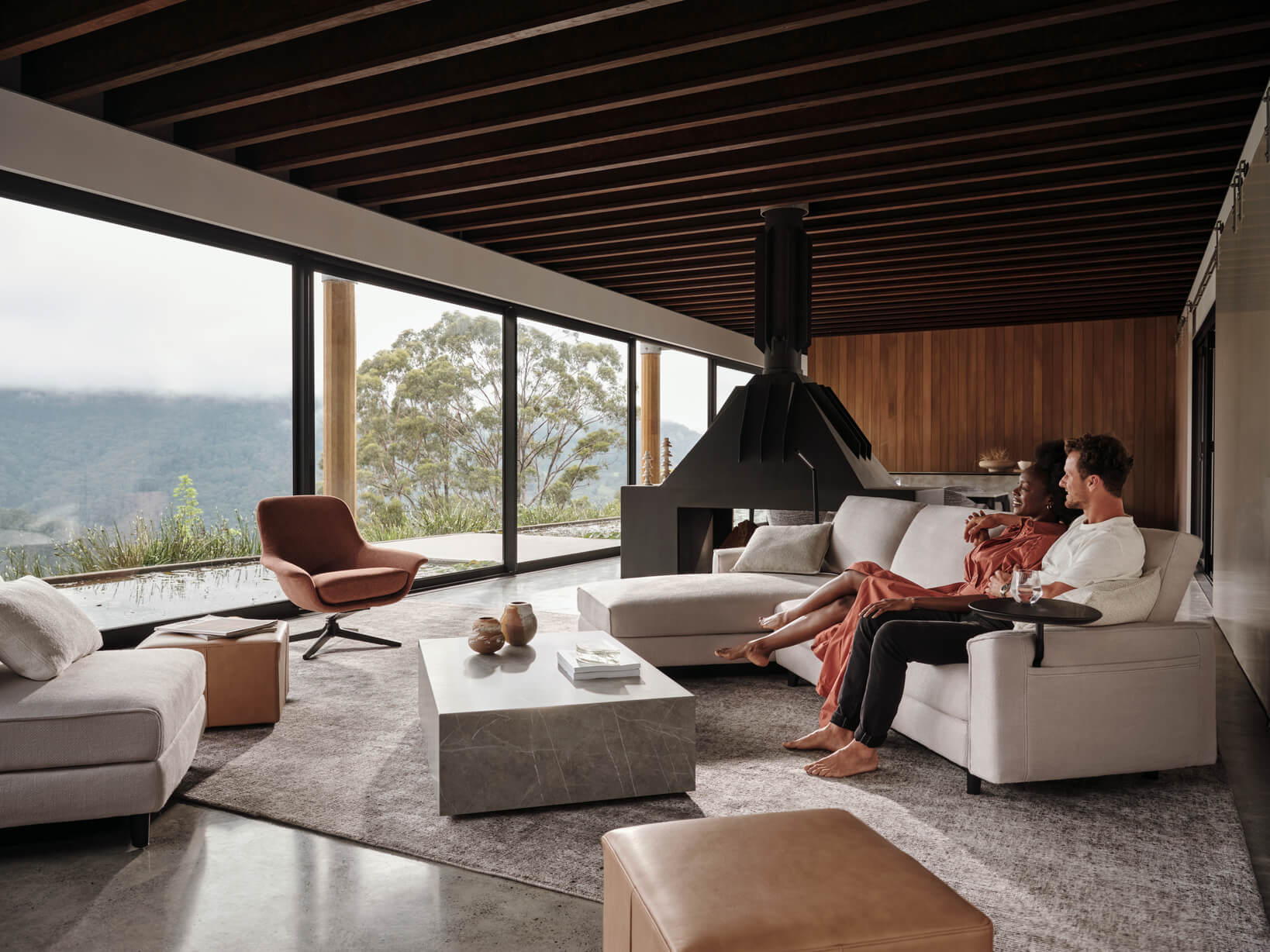 A couple relax on a contemporary, modular sofa in their home. The living room is warm and bright, minimally styled. 